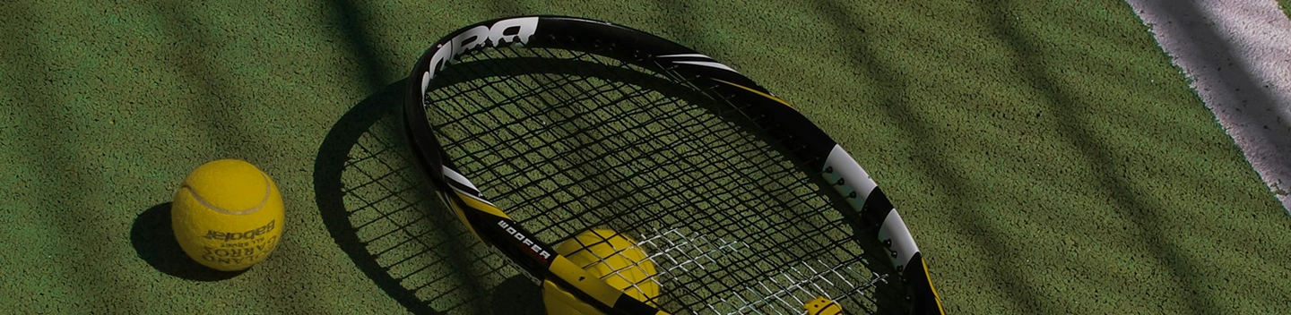 Une balle de tennis posée sur une raquette, avec un fond de court flou, immortalisant un moment sportif classique juste avant un service ou un échange.