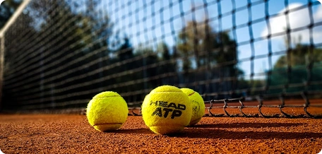 Des balles de tennis disposées près du filet sur un court en terre battue, illustrant les conditions de jeu professionnelles et la texture de la surface du court.