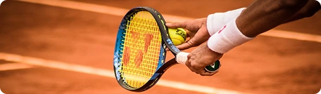 Un joueur de tennis s'apprêtant à servir avec sa raquette et sa balle sur un court en terre battue, une image qui rend compte de l'action et du mouvement dans le cadre d'un match de compétition.